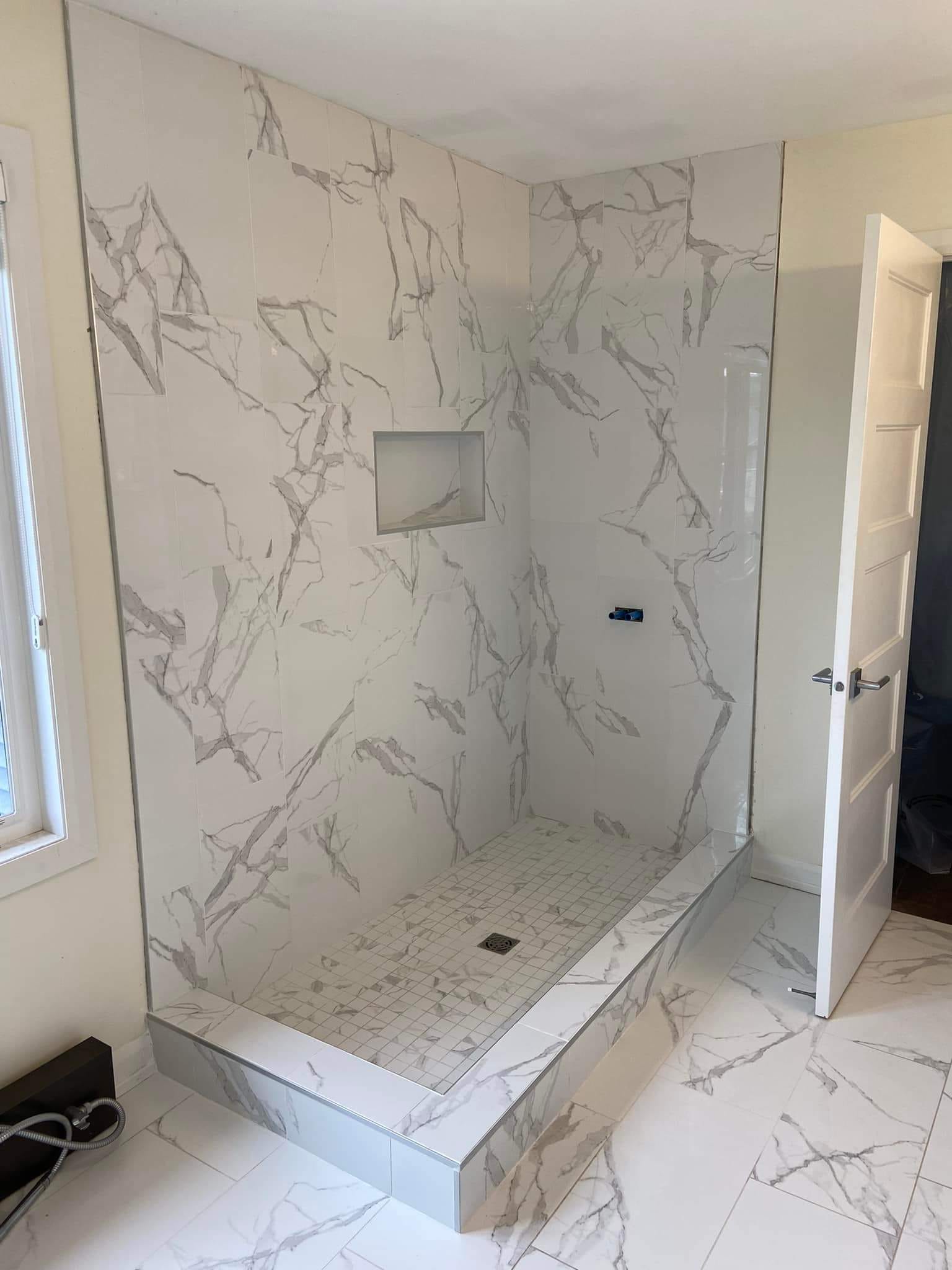 Bathroom during tiling — large-format marble-effect tiles and walk-in shower niche